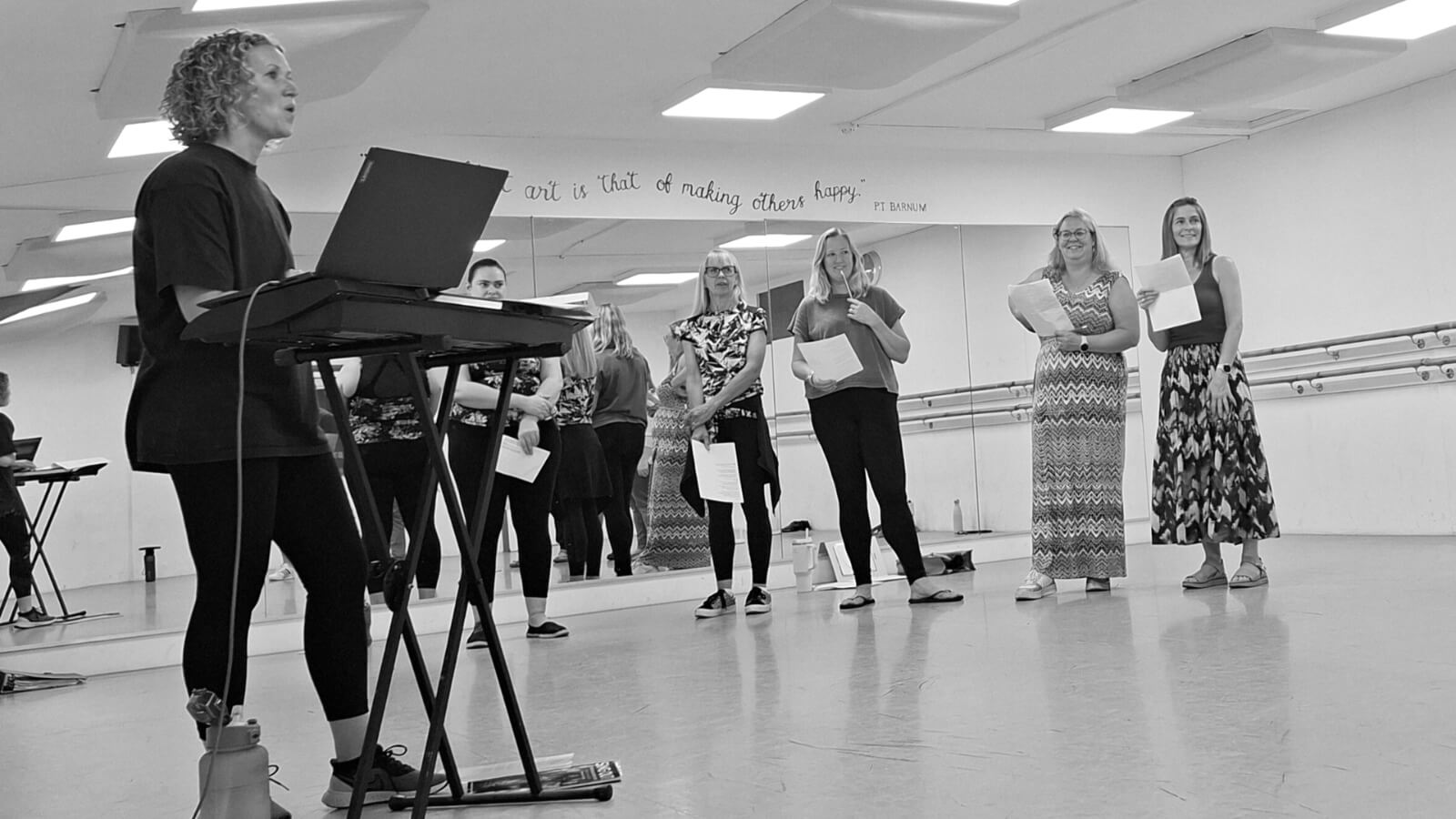 Monochrome photo of a group of women in a studio and one women standing in front of a keyboard