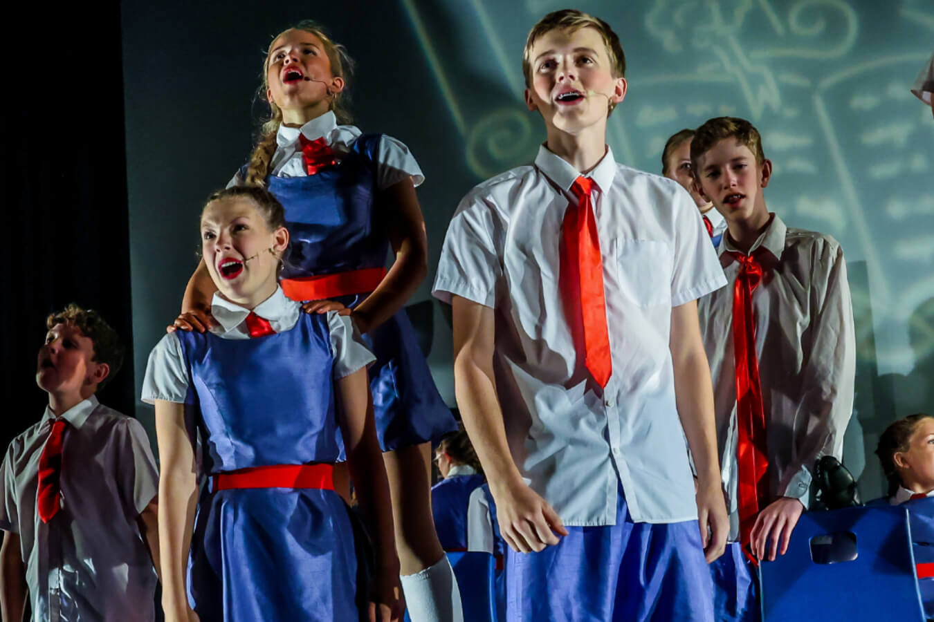 5 young people in school uniform singing and acting on stage during a performance